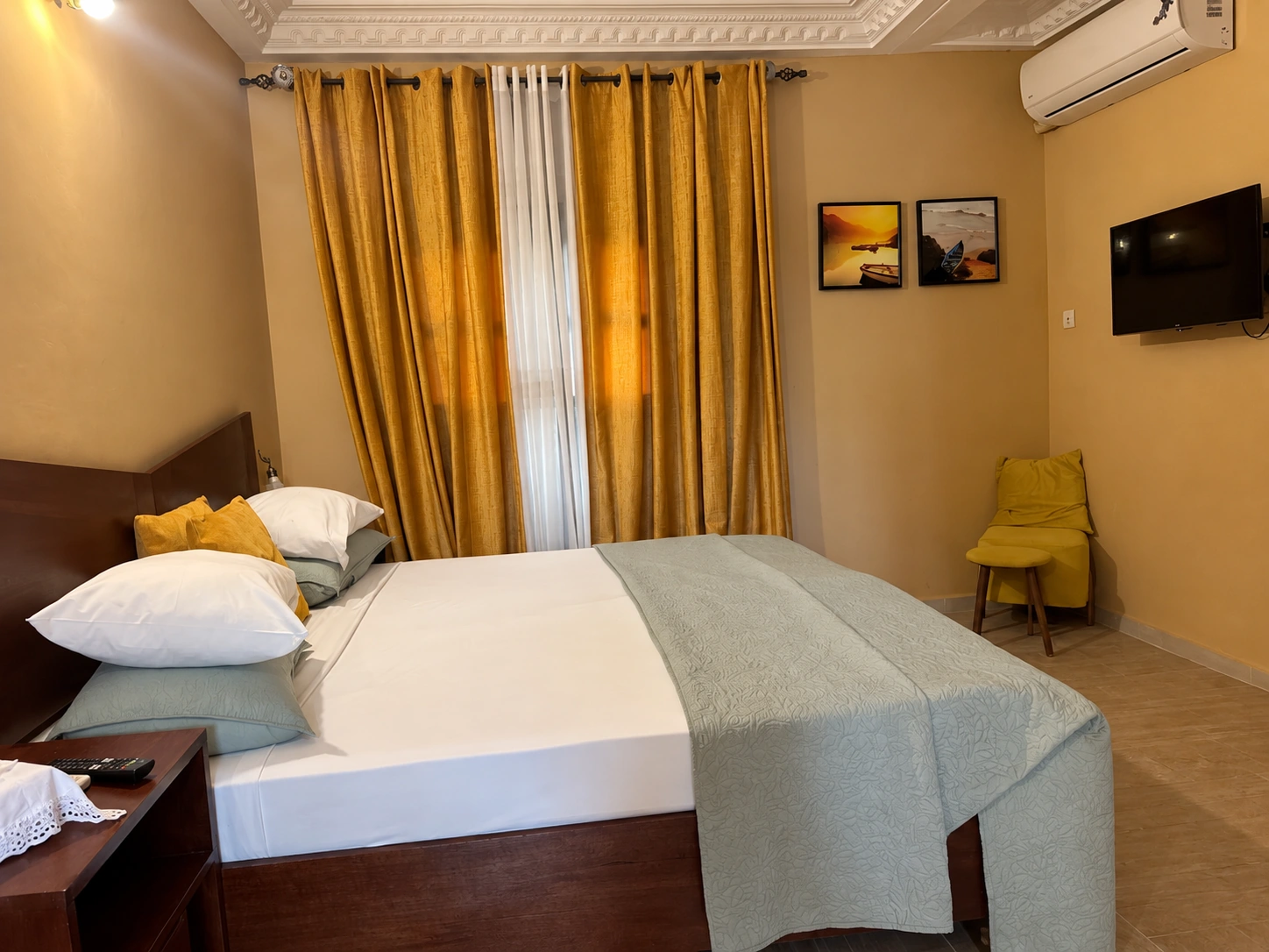 Chambre Standard avec rideaux dorés, lit et fauteuil jaune