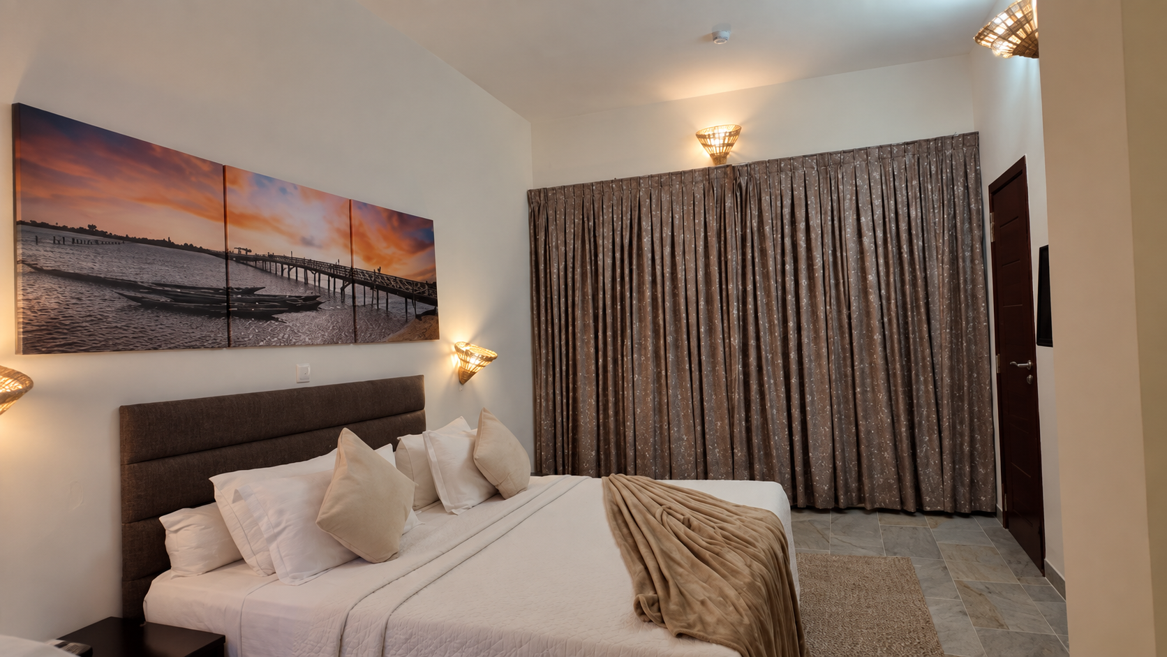 Chambre Deluxe réelle : literie beige et triptyque du pont au coucher du soleil